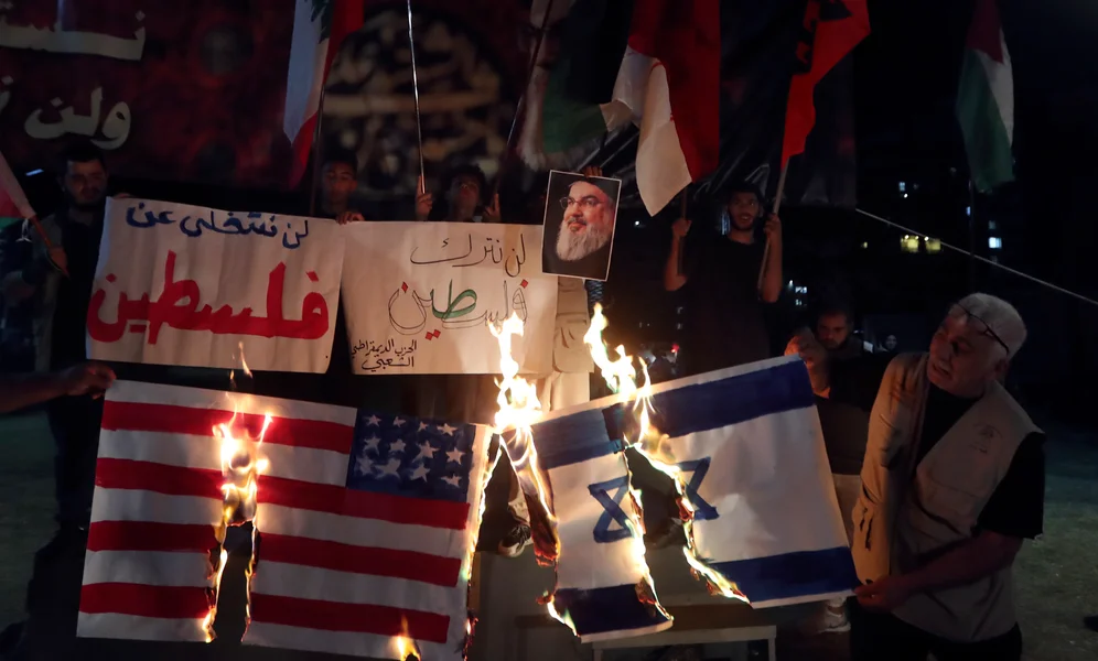 Lebanese and Palestinians burn a representation of the Israeli and U.S. flags during a commemoration marking the one-year anniversary of the Israel-Hamas war in the southern port city of Sidon, Lebanon, Monday, Oct. 7, 2024. Banner reads, "We will not abandon Palestine". (AP Photo/Mohammed Zaatari)